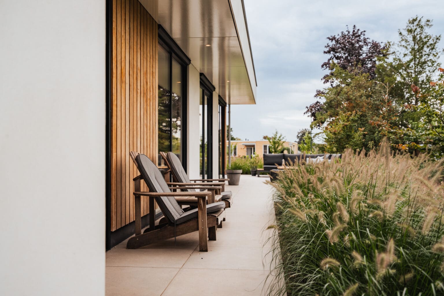 Terras langs de gevel met loungestoelen en siergrassen
